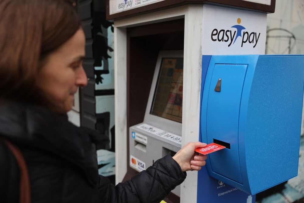 Мешканка Львова купує загальну ЛеоКарт в спеціальному терміналі EasyPay із функцією видачі карток. Вона рукою забирає з терміналу пластикову картку оранжево-червоного кольору із написом ЛеоКарт