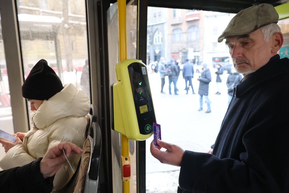 Чоловік прикладає до валідатора персоналізовану (синього кольору) ЛеоКарт у салоні громадського транспорту