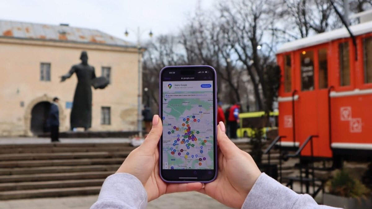 Дівчина тримає у руках телефон. На екрані - карта, де позначені безбар&rsquo;єрні заклади та місця. Позаду видно пам'ятник Івану Федоровичу