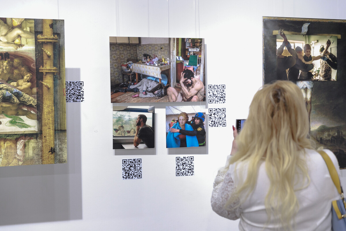 На стіні висять зображення та Qr-коди. Жінка фотографує.