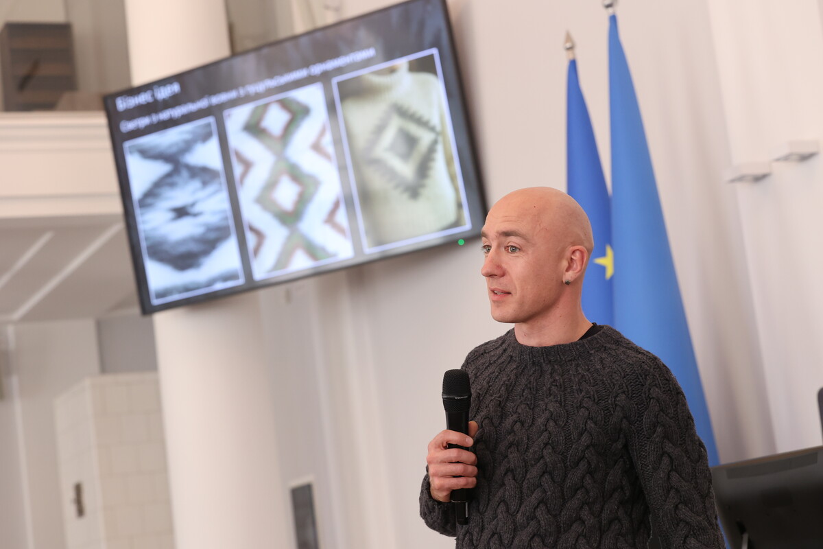Ветеран Микола Глібович розповідає про свій бізнес- проект. На екрані светри з вовни.