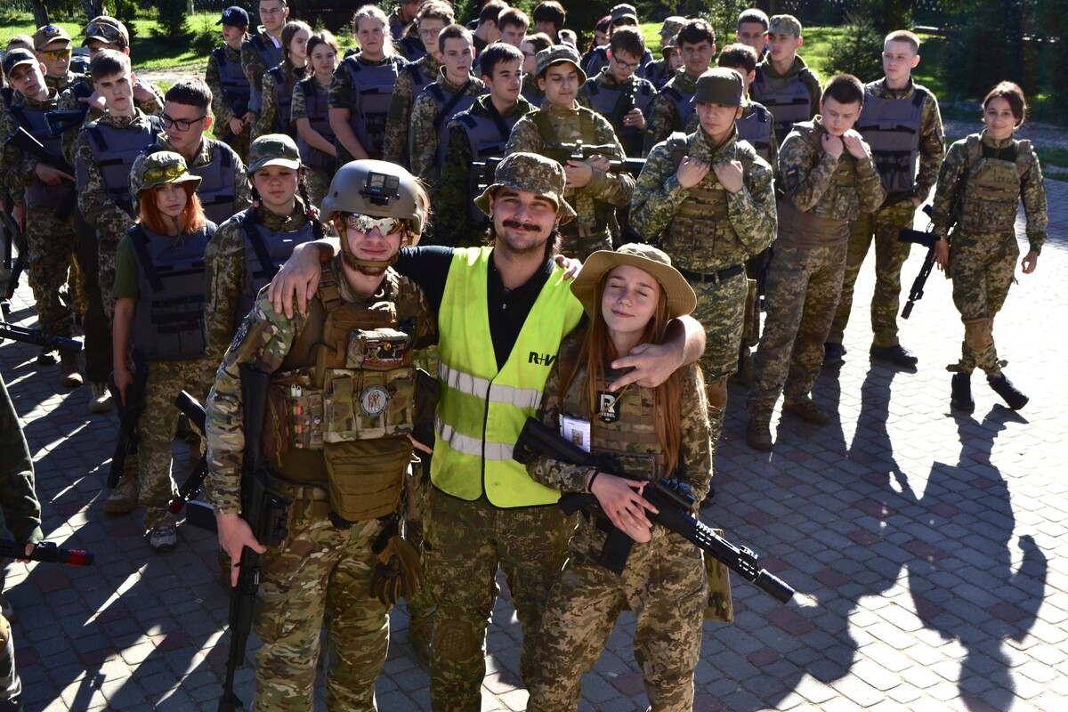 Групове фото учасників вишколу. У центрі - двоє усміхнених підлітків у камуфляжі та інструктор у жовтому жилеті