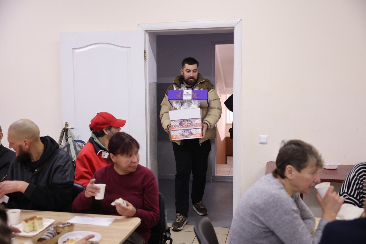 Богдан Іванусь, начальник відділу професійної освіти департаменту освіти та культури ЛМР тримає у руках коробки з солодким. У їдальні за столами частуються люди.