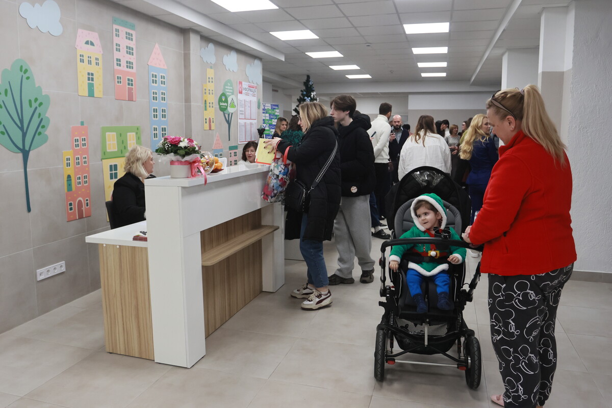 Біля рецепції центру багато відвідувачів, на передньому плані є жінка з дитячим візком