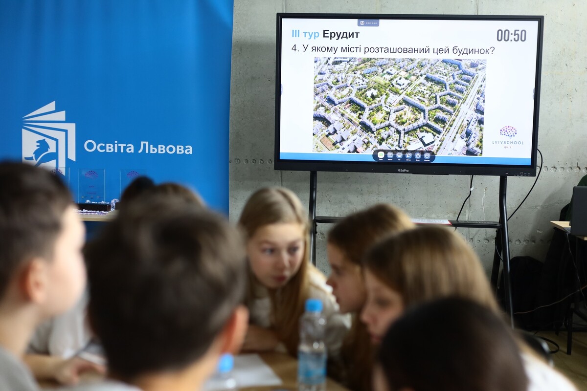 Учні обговорюють завдання. Позаду - мультиборд, на екрані якого напис &ldquo;Третій тур Ерудит&rdquo;.