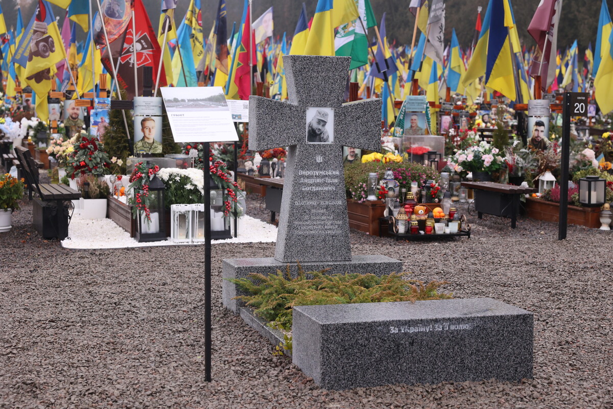 зразок пам&rsquo;ятника, зробленого з граніту, сірого кольору з чорно-білою фотографією воїна. Позаду - могили з прапорами.
