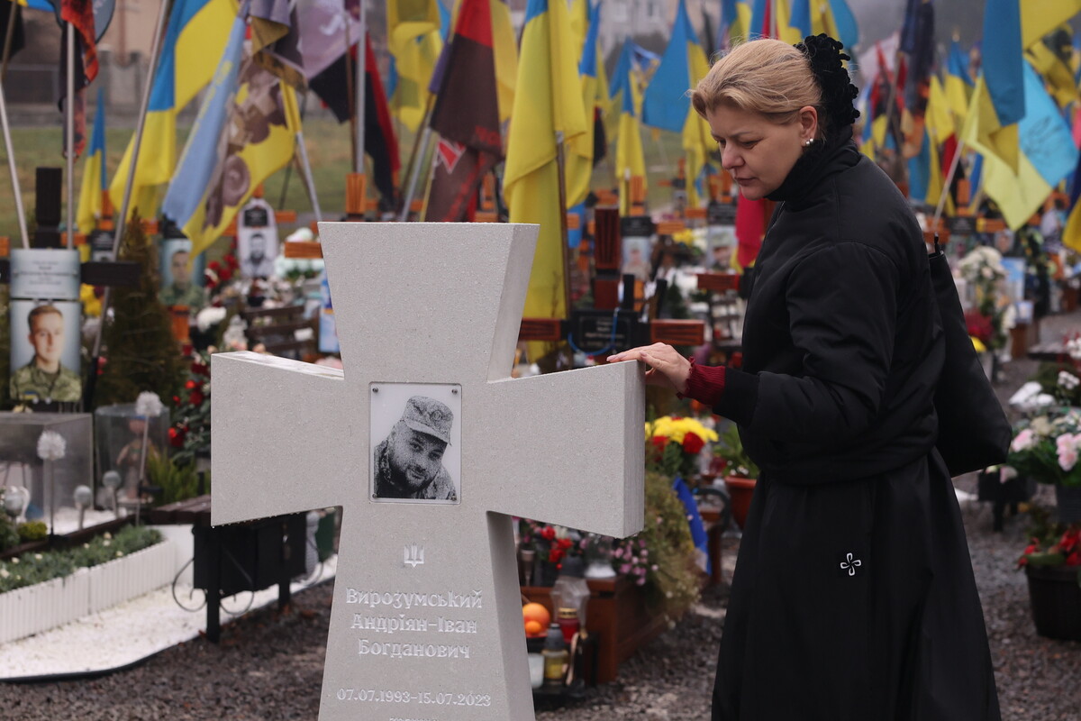 дружина полеглого захисника торкається одного зі зразків хреста. Позаду видно прапори на могилах воїнів.