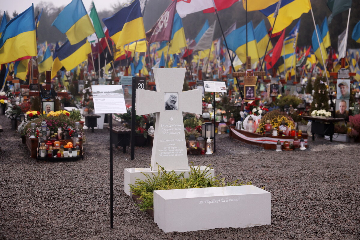 зразок пам&rsquo;ятника, зробленого у матеріалі - тераццо, світлого кольору з чорно-білою фотографією воїна. Позаду - могили з прапорами.