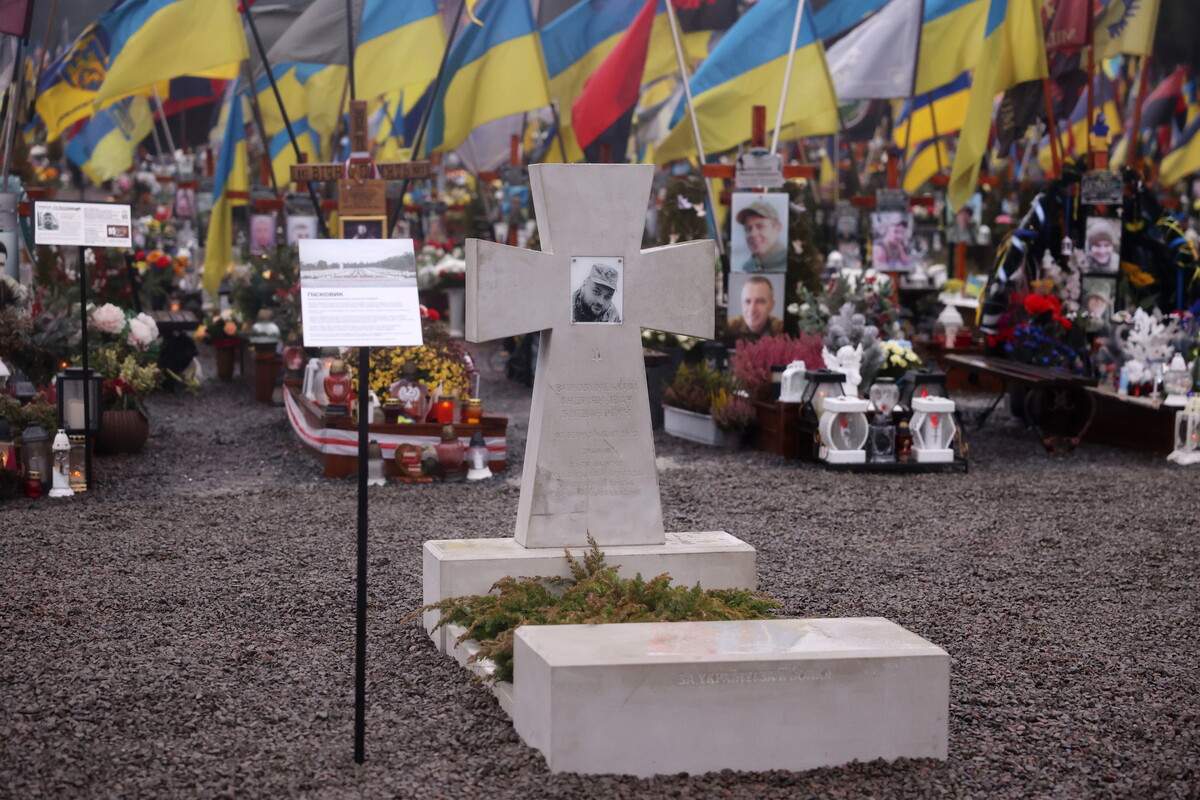 зразок пам&rsquo;ятника, зробленого з пісковика, світлого кольору з чорно-білою фотографією воїна. Позаду - могили з прапорами.
