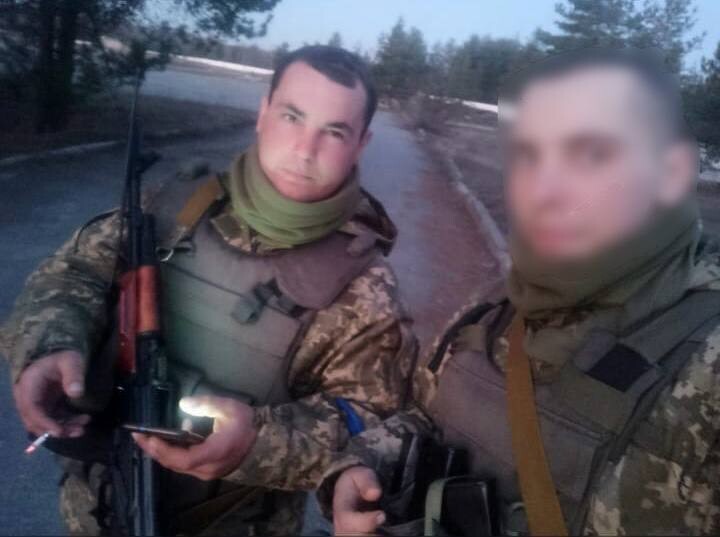 Денис Кочерга під час служби у військовій формі зі зброєю. Поруч з ним побратим із заблюреним обличчям. Довкола &ndash; дерева