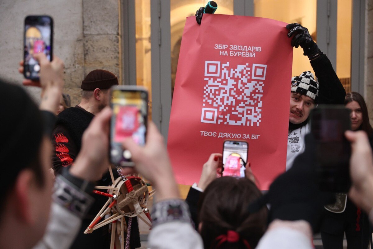Організатор спільноти &laquo;СHUMAKY&raquo; тримає плакат з Qr-кодом збору на військо та надписом "Збір Звіздарів на Буревій". Учасники забігу фотографують зображення