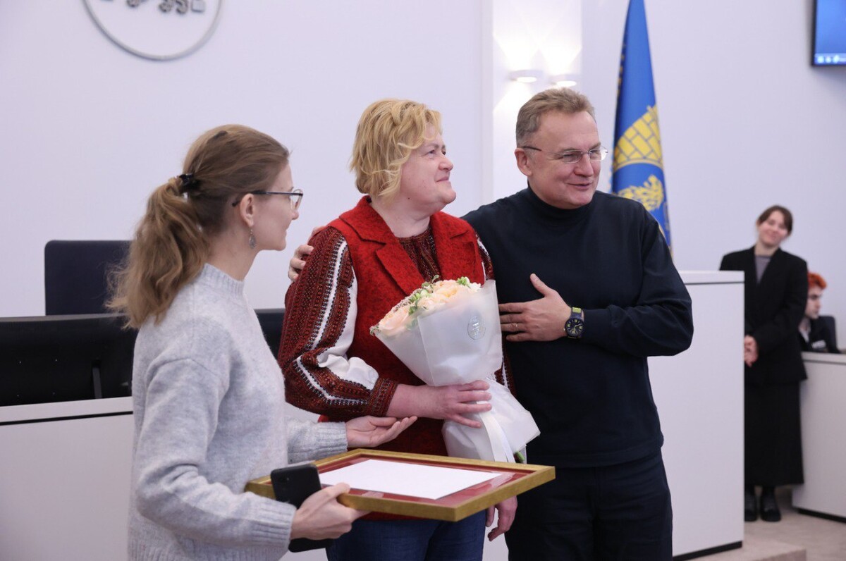 Мер Львова Андрій Садовий обіймає Оксану Потимко. Жінка з квітами в руках усміхається. Поруч з нею дівчина тримає подяку.