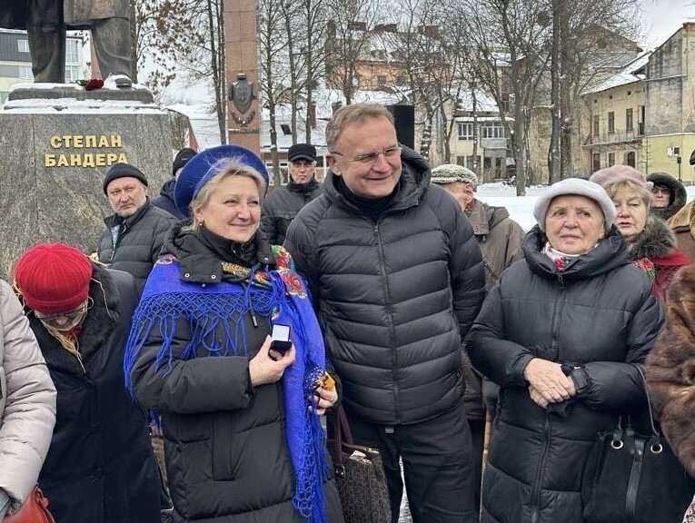 Мер Львова Андрій Садовий стоїть поруч із Ореславою Хомик, яка тримає у руках коробочку із знаком &laquo;Прапор України&raquo;. Позаду видно пам'ятник Степану Бандері. Поруч багато людей