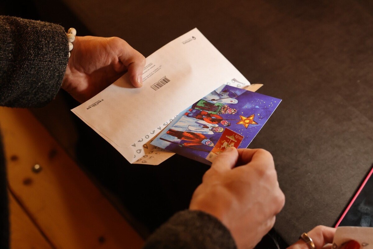 Людина, обличчя якої не видно, вкладає в конверт святкову листівку із зображеннням українського вертепу