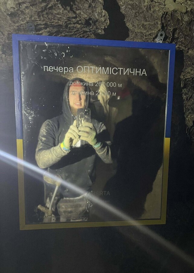 Ветеран Віктор Драчук фографується у печері у дзеркалі, на якому є написи: печера ОПТИМІСТИЧНА, довжина 267 000 м, глибина 20-80 м