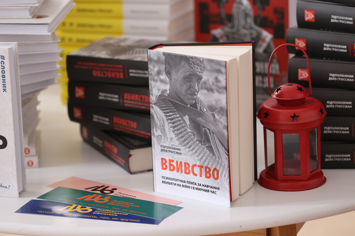 книга &laquo;Вбивство&raquo; підполковника Девіда Ґроссмана. Позаду й збоку видно стоси інших примірників цієї ж книги з чорними обкладинками та червоними акцентами. Праворуч від книги стоїть декоративний червоний ліхтар із зіркоподібними прорізами.