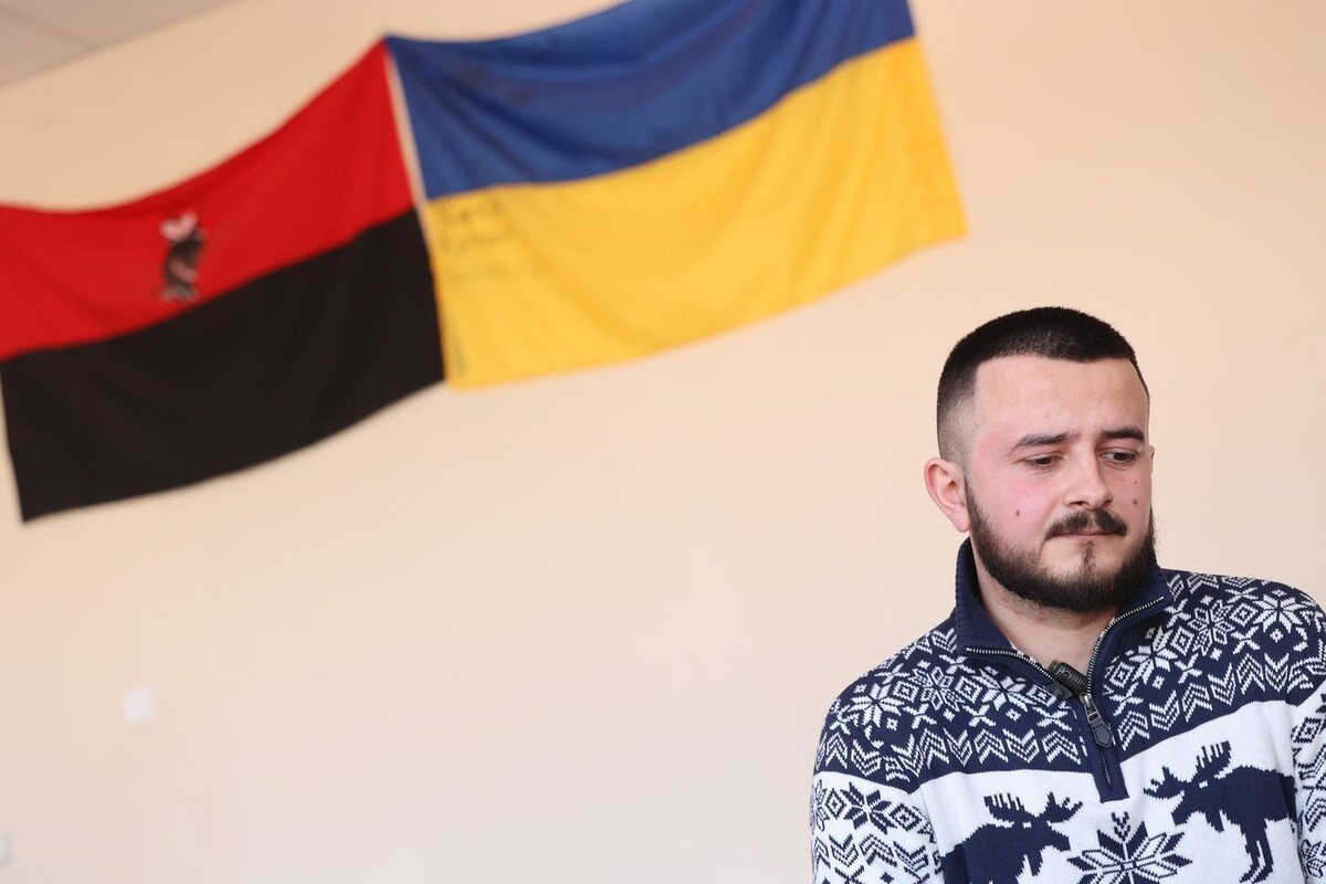 Ігор Дусан, на стіні позаду висять синьо-жовтий та червоно-чорний прапори
