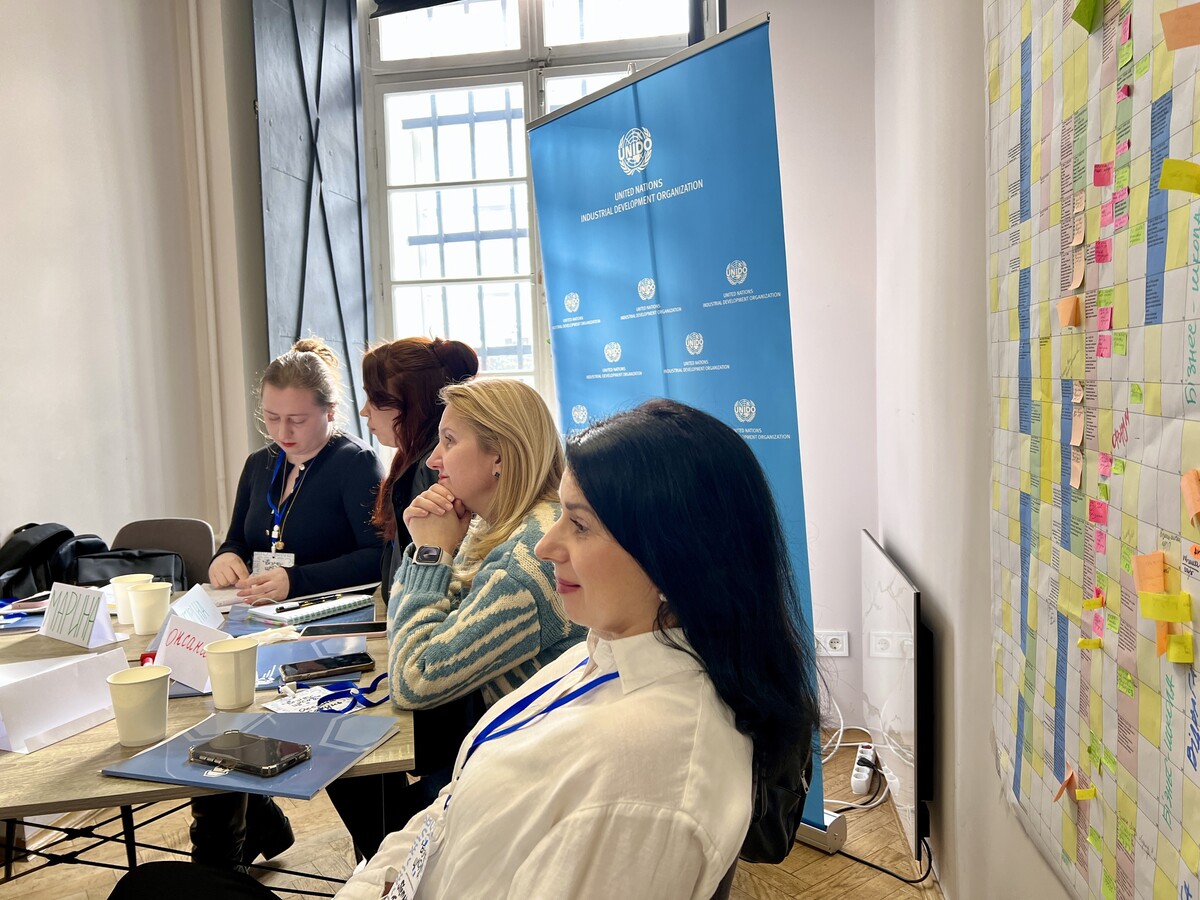 Четверо учасниць Бізнес-школи за партою під час навчання. Позаду них плакат з емблемою донорів UNIDO