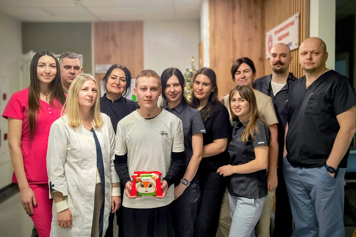 Спільне фото пацієнта та лікарів, які його лікували; всі усміхаються, хлопець тримає в руках тортик