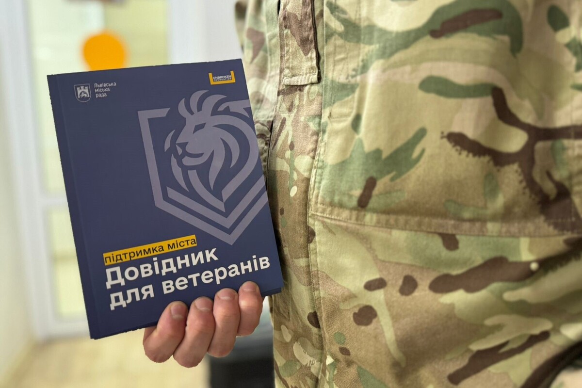 Хтось у військовій формі тримає в руці невеличку книжку синього кольору з назвою "Довідник для ветеранів"