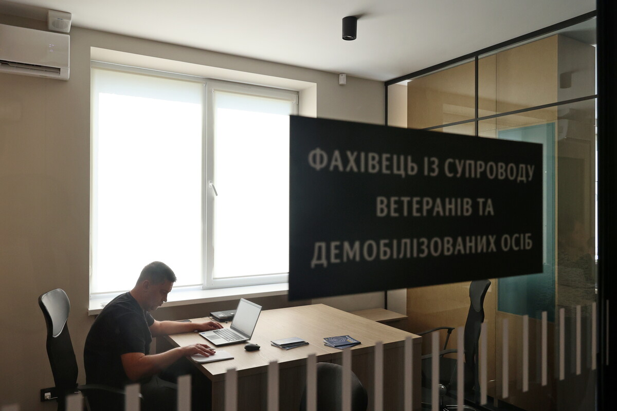 Через скляні двері видно світлу кімнату, де за столом сидить чоловік і щось записує. На дверях напис "Фахівець із супроводу ветеранів та демобілізованих осіб"