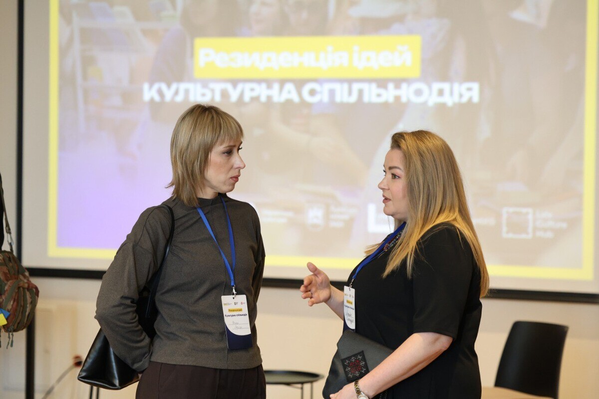 Зліва Оксана Маркіна, директорка КЗ «Слобожанська школа мистецтв» розмовляє із Онищук Маєю, директоркою Хмельницького обласного науково-методичного центру культури і мистецтва. Позаду видно екран із написом “Культурна спільнодія”.