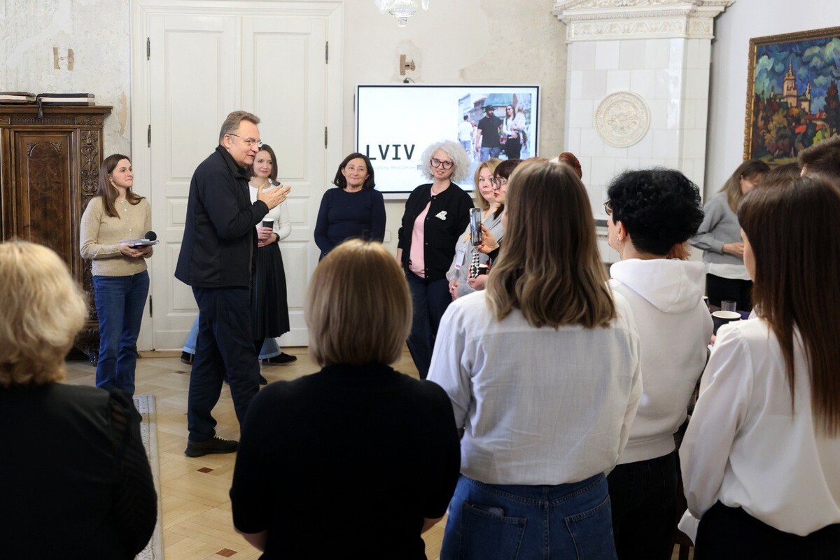 Міський голова Андрій Садовий говорить з учасниками резиденції, які стоять півколом, у кабінеті мера. Позаду на екрані презентація з написом "LVIV"