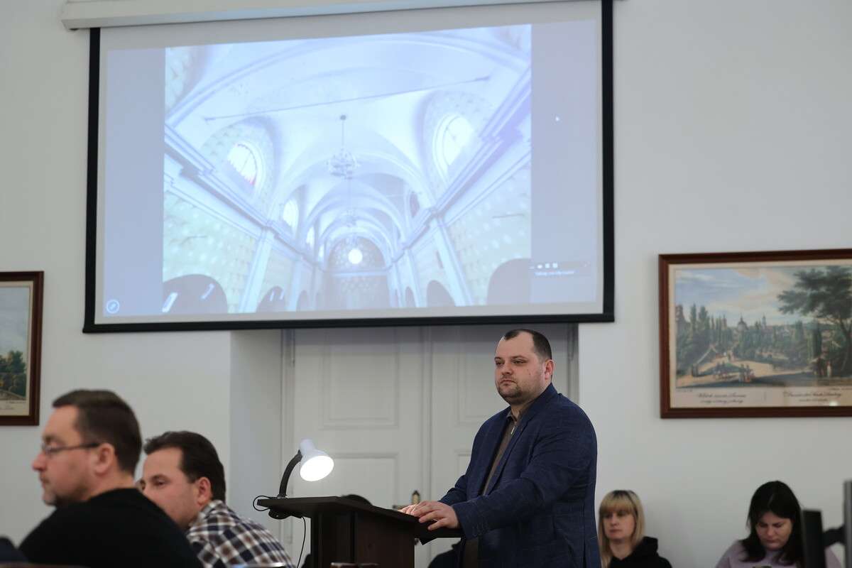 Святослав Кіндратів доповідає на засіданні виконавчого комітету: він стоїть перед трибуною, вгорі &ndash; великий екран, на якому є кадр, як виглядає монастир всередині