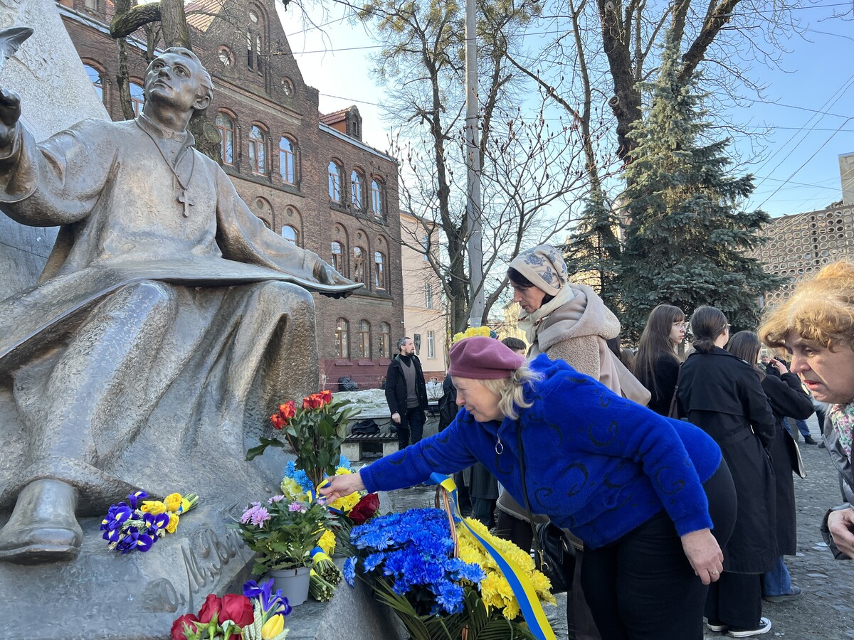 Жінка у синьому светрі кладе квіти до підніжжя пам&rsquo;ятника Михайлу Вербицькому. Поруч зібралися люди, які також прийшли вшанувати пам&rsquo;ять, а біля монумента видно багато букетів у синьо-жовтих кольорах.