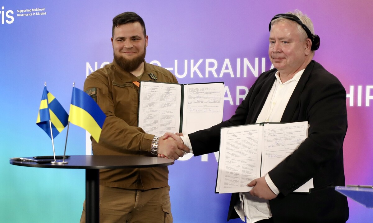 На сцені форуму представники міст Нововоронцовка і Тьорн тримають у руках щойно підписаний меморандум про співпрацю. Перед ними стіл, на якому стоять прапори України та Швеції
