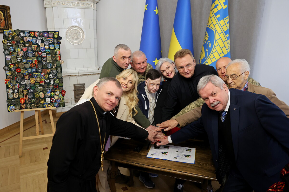 Капелан Львівської міської ради Андрій Сіданич, співачка Ірина Федишин, генерал-майор Борис Генов, секретар Львівської міської ради та військовослужбовець Маркіян Лопачак, львів&rsquo;янин, який пережив ракетний удар, Роман Олексів, мисткиня і перша леді Львова Катерина Кіт-Садова, мер Львова Андрій Садовий, полковник Роман Качур, Почесні громадяни Львова Мирослав Маринович та Андрій Содомора під час погашення марки.