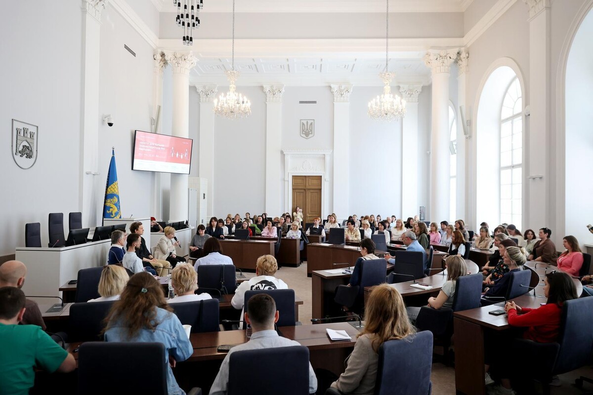 Велика зала у Міській раді наповнена людьми. По центру сидять спікери. Навколо учасники події уважно їх слухають