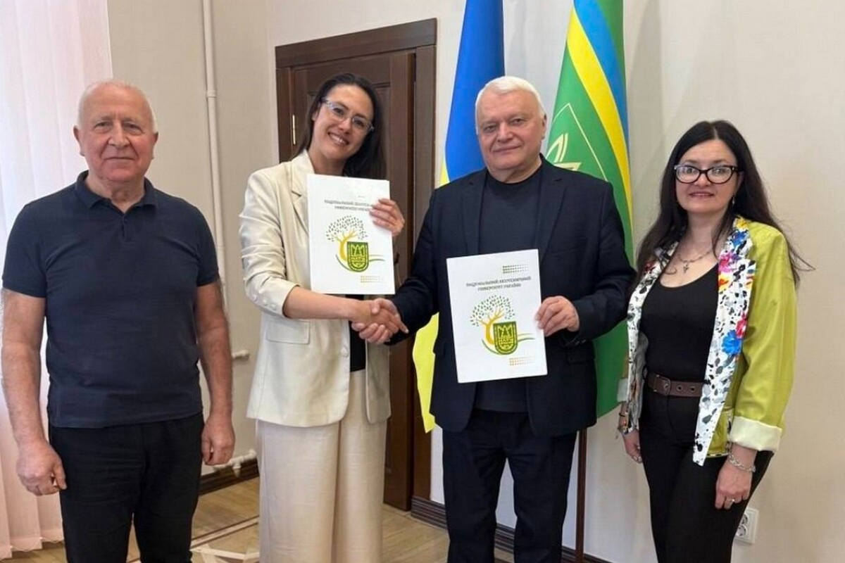 Представники управління екології Львова та Лісотехнічного університету України під час підписання договору про співпрацю. Учасники заходу тримають підписані документи та символічно тиснуть руки на тлі українського та університетського прапорів
