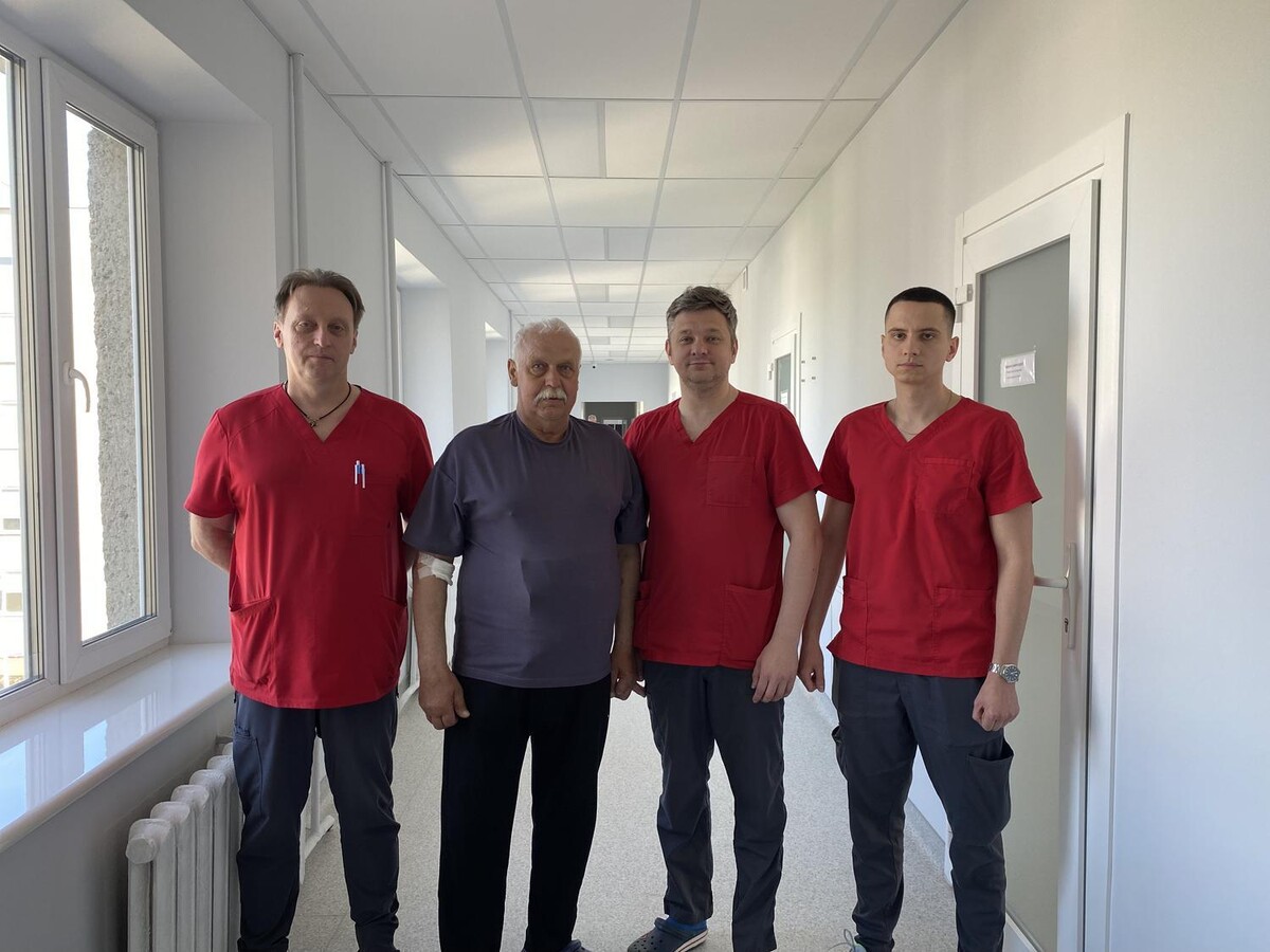 Пацієнт у синій футболці та троє лікарів в червоній медичній формі на коридорі медзакладу