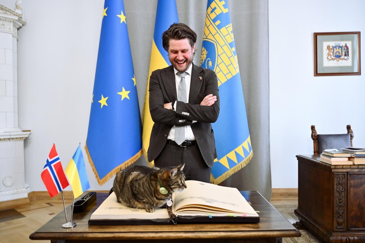 Державний секретар Міністерства торгівлі, промисловості та рибальства Норвегії після підписання книги почесних гостей. Він стоїть та усміхається. На книзі лежить котячий мер Львова Левчик