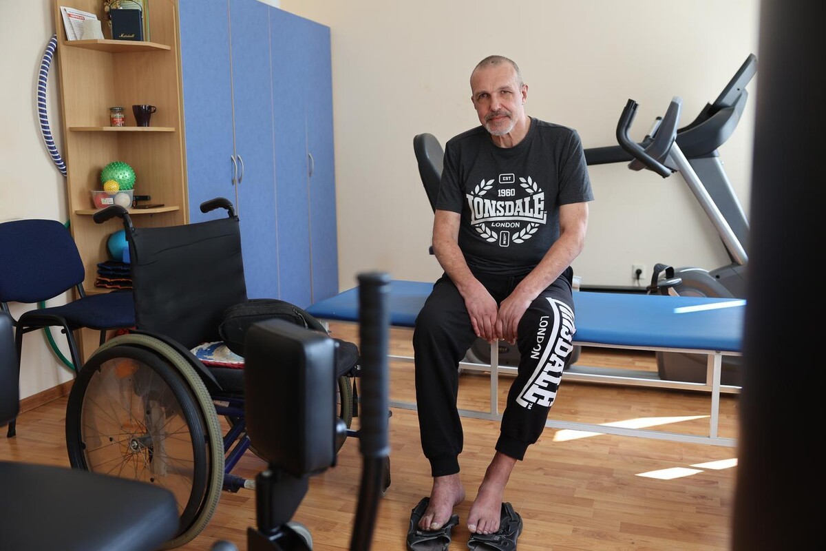 Юрій Альошин сидить на кушетці в реабілітаційному залі. Поруч стоїть крісло колісне, позаду видно реабілітаційне обладнання.