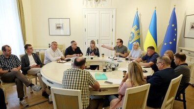 Засідання робочої групи щодо території Львівського автобусного заводу. Більше десятка осіб - посадовці та депутати Львівської міської ради - сидять за великим круглим білим столом та обговорюють питання. Позаду зправа видно прапори Львова, України та ЄС