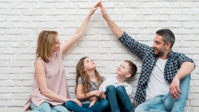 Батьки і діти сидять усміхнені на підлозі. Діти дивляться вгору на руки батьків. Фото ілюстративне.