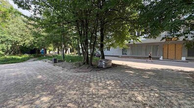 Територія на вулиці Роксоляни у Львові поруч з майбутнім ЦНАПом та простором для ветеранів. На фоні будівля, де триває ремонт. Перед нею територія без елементів доступності. Збоку видно дерева та зелень
