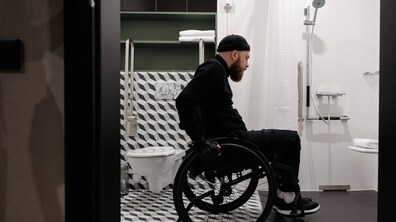 Чоловік на кріслі колісному оглядає ванну кімнату в апартаментах готелю. Фото апартготелю TULIP