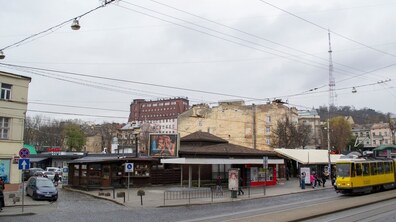 МАФи перед колишнім ринком «Добробут», поруч зупинка громадського транспорту, де зупинився жовтий трамвай. З лівого боку припаркована машина
