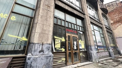 Фасад будинку з великими вікнами та центральними дерев’яними дверима, обрамленими кам’яними декоративними елементами - це приміщення на вул. Гнатюка, де колись довгий період розташовувалися залізничні каси. На стінах і вікнах жовтим кольором намальовані графіті