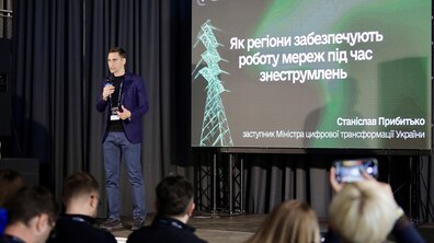 Станіслав Прибитько, заступник міністра цифрової трансформації України, виступає з мікрофоном перед аудиторією біля екрана з презентацією про роботу мереж під час знеструмлень