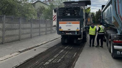 Процес ремонту дороги на вул. Кондукторській. У центрі кадру — велика сіра дорожня фреза, яка рухається вперед і зрізає старий асфальт, залишаючи за собою широку темну смугу. Справа від техніки стоять двоє робітників у яскравих салатових світловідбивних жилетах, а поруч частково видно вантажівку.