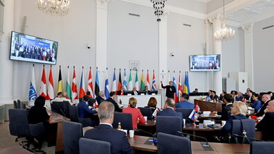 Зустріч у великій сесійній залі ЛМР за участі представників різних країн. Учасники сидять за столами та слухають виступ міського голови Андрія Садового. У залі прапори держав-учасниць та міжнародних організацій.