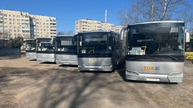 Пять великих сріблястих автобусів стоять на відкритому майданчику, на кожному з них видно логотип італійської компанії TUA. На другому плані - багатоповерхові житлові будинки та безхмарне небо