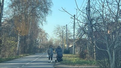 дві жінки, одна з дитячою коляскою, ідуть по проїзній частині дороги на вул. Білогорща