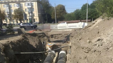 Роботи із заміни магістральної теплової мережі на вул. Науковій. Неподалік розриття кілька працівників монтують нову чорну трубу, яку згодом протягнуть усередину металевої труби більшого діаметра, що лежить поруч. Біля місця робіт стоять екскаватор і вантажівка.