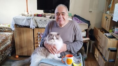 Усміхнений пан Богдан сидить у квартирі, на руках тримає кота