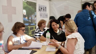 Жінки у білому наметі сидять за столом і заповнюють документи